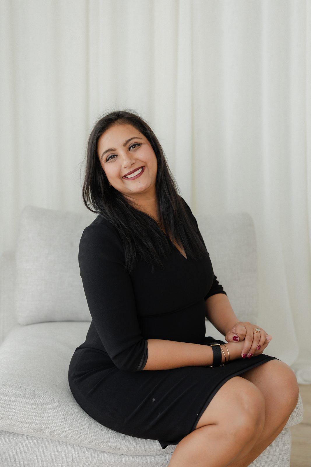 Sugandha Arora, insurance adviser and health professional in Hamilton, smiling on a couch